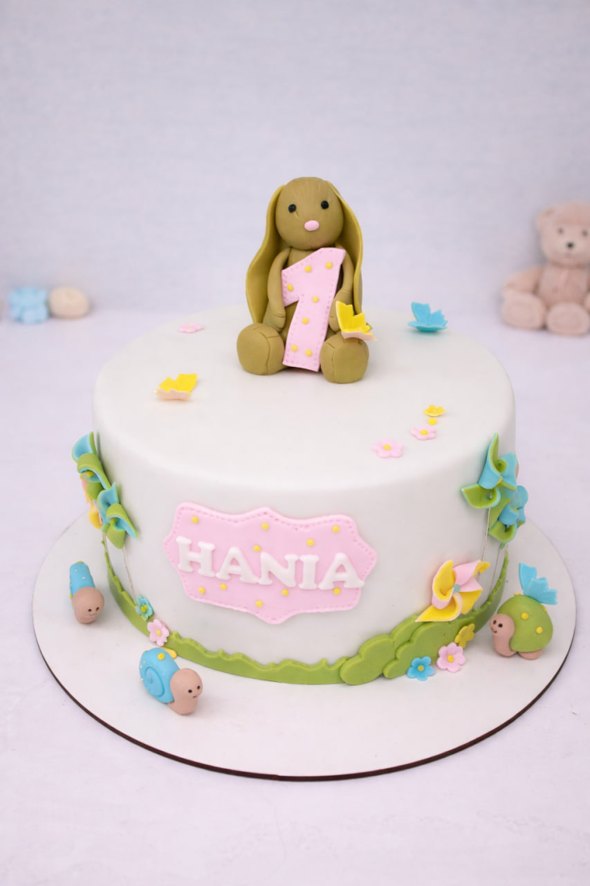 tort z króliczkiem trzymającym jedynkę, biały fondant, pastelowe kwiatki, tabliczka z imieniem Hania
